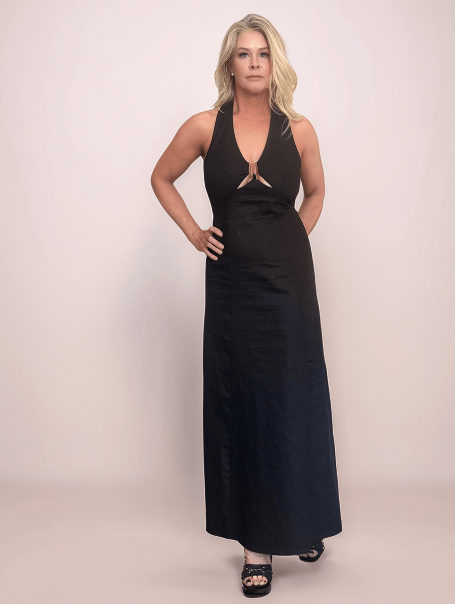 A blonde woman wearing a black linen halter cutout maxi dress with a gold ring detail at the bust. Perfect for summer events and resort wear