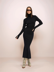 Woman wearing a black turtleneck dress and floral shoes on a light pink background
