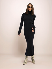 Woman wearing a black long-sleeve dress and sunglasses on a beige background