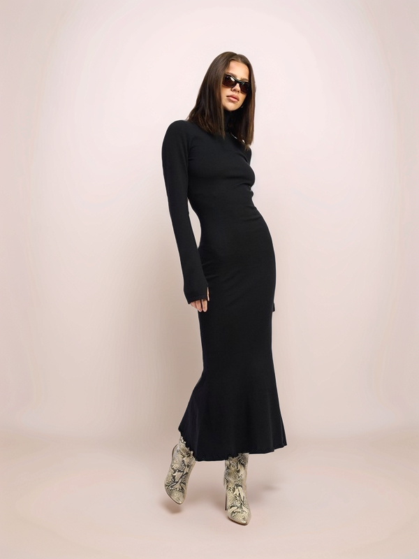 Woman wearing a black dress with long sleeves and a slit on a light pink background