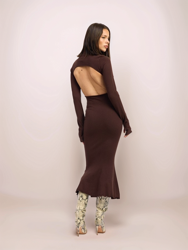 Woman wearing a brown long-sleeve dress with a slit, standing against a plain background.