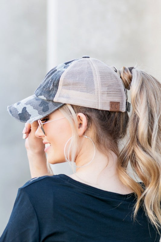 Woman wearing a camouflage baseball cap with a mesh back against a plain background