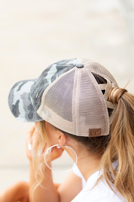 Person wearing a camouflage baseball cap with a mesh back, listening to music with earphones.