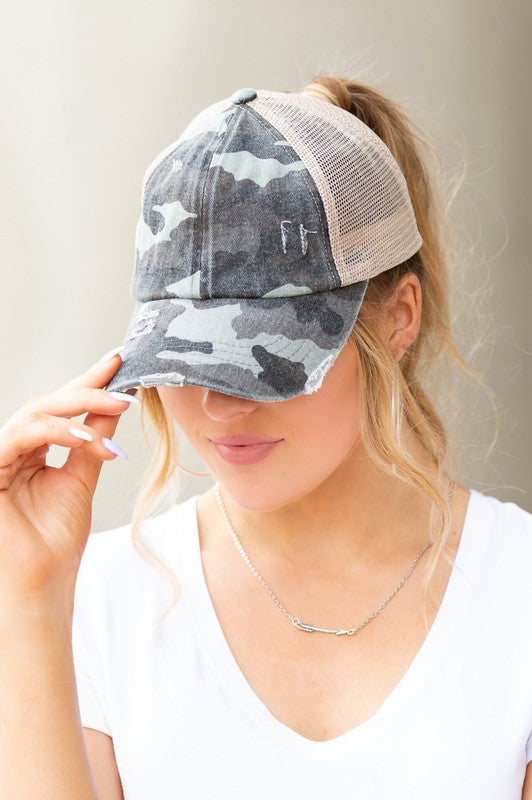 Woman wearing a camouflage trucker hat with a neutral brim against a plain background