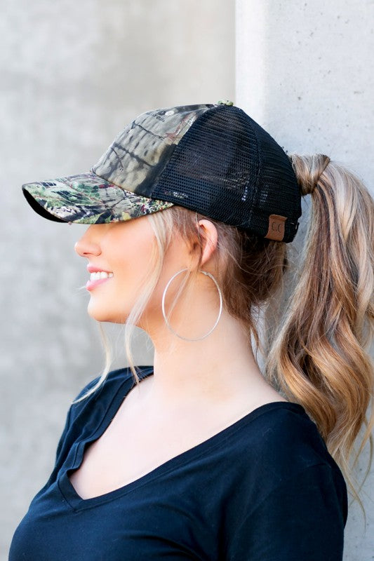 Woman wearing a camouflage and black cap against a gray wall