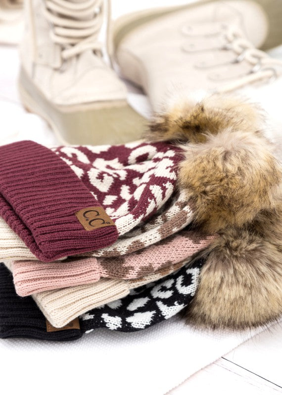 Stack of knitted beanie with a fur pom on a light surface
