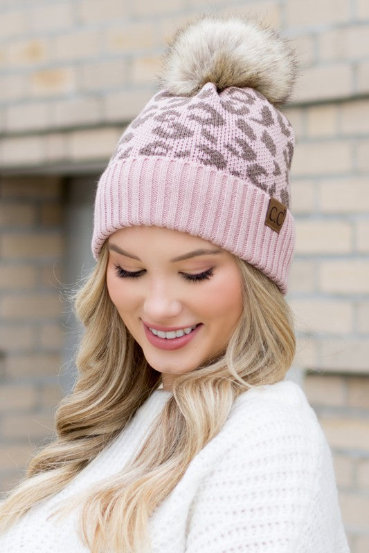 Woman wearing a pink patterned beanie with a fur pom-pom outdoors.