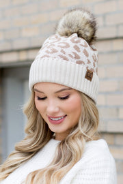 Woman wearing a patterned beanie with a fur pom-pom outdoors.