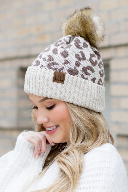 Person wearing a leopard print beanie with a pom-pom and a visible brand logo.