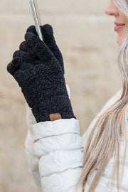 Person wearing black gloves with a brand logo, holding a metallic object against a neutral background