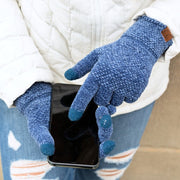 Person wearing blue fleece gloves holding a phone, with a white jacket and patterned pants.
