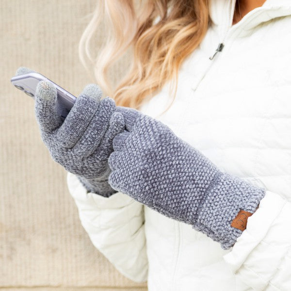 Person wearing gray fleece gloves using a smartphone indoors.