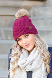 Woman wearing a pink knit beanie with a pom-pom and a white scarf, standing on steps.