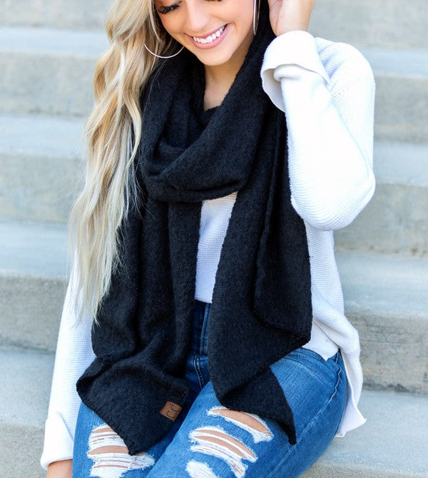 Woman wearing a black scarf, white sweater, and blue jeans sitting on steps.