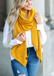 Woman wearing a mustard yellow scarf, white sweater, and blue jeans outdoors.