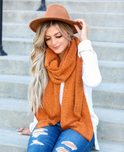 Woman wearing a brown hat and orange scarf sitting on steps.
