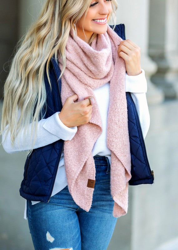 Woman wearing a pink scarf, navy vest, and blue jeans outdoors.