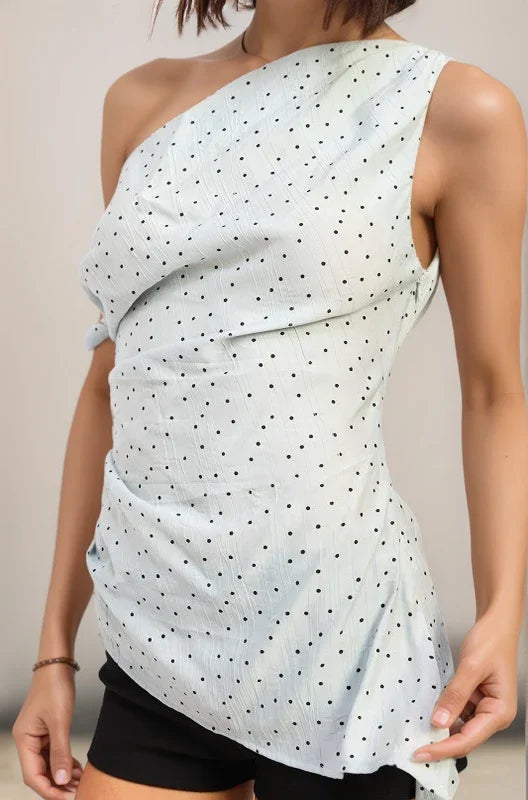 Woman wearing the celeste light blue one-shoulder top with black polka dots against a beige background