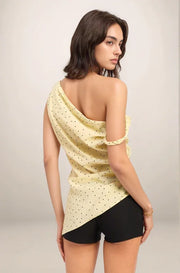 Woman wearing the celeste one shoulder yellow polka dot top and black shorts on a plain background