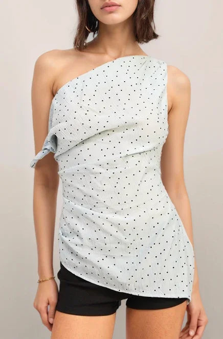 Woman wearing the baby blue one-shoulder polka dot top and black shorts against a plain background