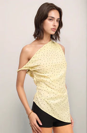 Woman wearing a yellow one-shoulder top with black polka dots and black shorts on a light gray background