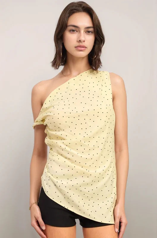 Woman wearing the yellow celeste one-shoulder top with black polka dots on a plain background