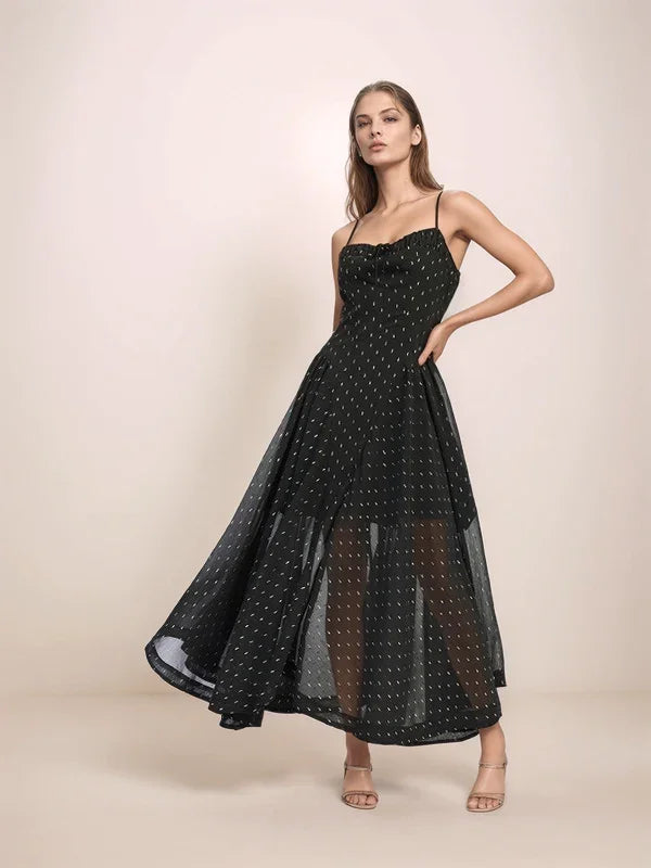 Woman wearing a black sheer dress with silver polka dots on a beige background