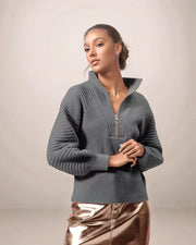 Woman wearing a gray zip-up sweater against a plain background