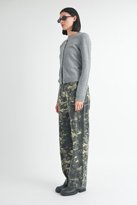 Person wearing a gray cardigan and camouflage pants on a white background