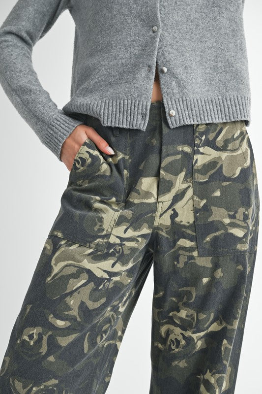 Person wearing a gray cardigan and camouflage pants on a light gray background