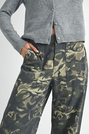 Person wearing a gray cardigan and camouflage pants on a light gray background