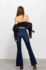 Woman wearing a black off-shoulder top and blue flared jeans against a white background