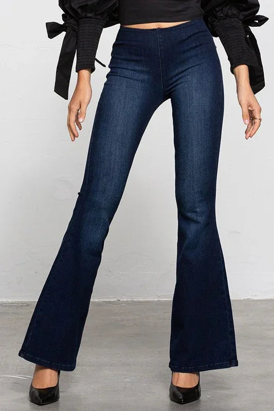 Person wearing dark blue flared jeans with a plain background