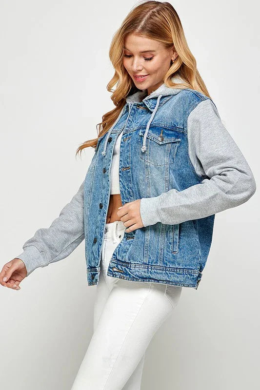Woman wearing a denim jacket over a gray hoodie with white jeans on a white background 