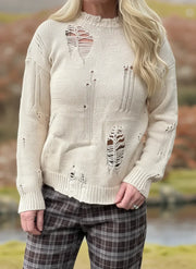 Person wearing a distressed cream sweater with plaid pants outdoors.