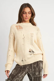 Woman wearing a beige distressed sweater on a plain background