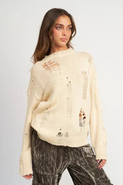Woman wearing a beige distressed sweater against a plain background