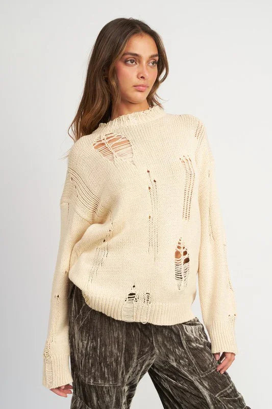 Woman wearing a beige distressed sweater against a plain background