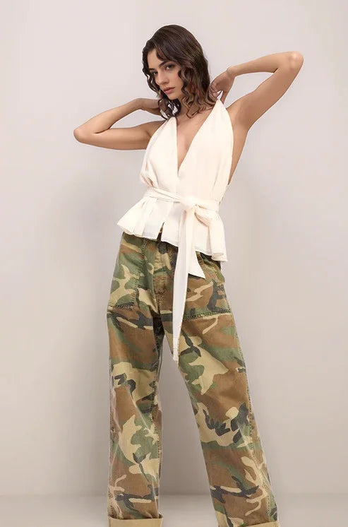 Woman wearing the elysian halter top in white and camouflage pants against a plain background