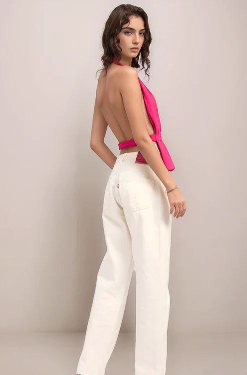 Woman wearing the elysian hot pink halter top and white pants against a plain background