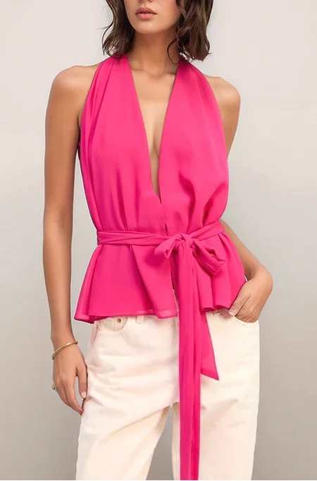 Woman wearing a bright pink halter top with a deep neckline and white pants on a plain background