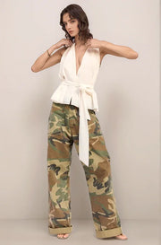Woman wearing the elysian white top and camouflage pants against a plain background