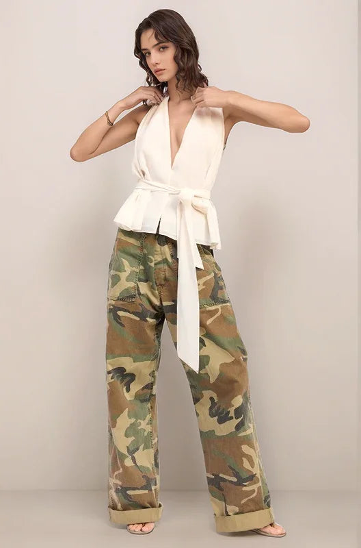 Woman wearing the elysian white top and camouflage pants against a plain background