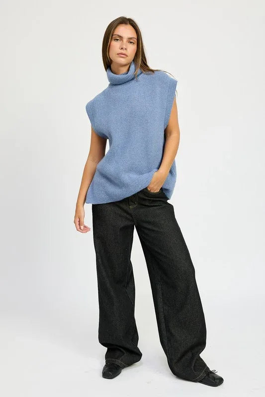 Person wearing a blue sleeveless sweater and black pants on a white background