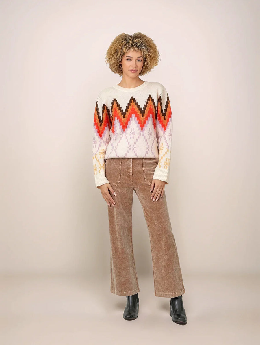 Person wearing a colorful sweater and brown pants on a plain background