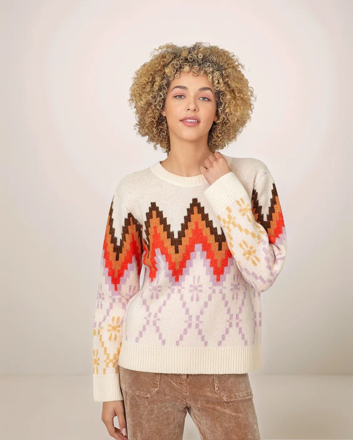 Woman wearing an orange and brown colorful patterned sweater against a plain background