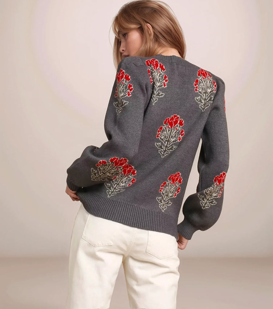 Person wearing a gray sweater with floral patterns on a plain background
