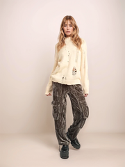 Woman wearing a cream sweater and patterned pants on a beige background
