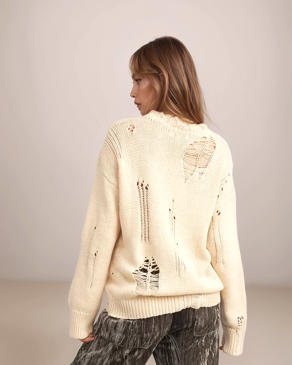 Woman wearing a cream-colored distressed sweater against a plain background