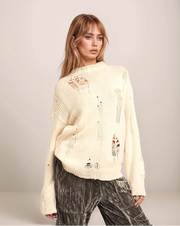 Woman wearing a cream-colored sweater with unique patterns on a plain background